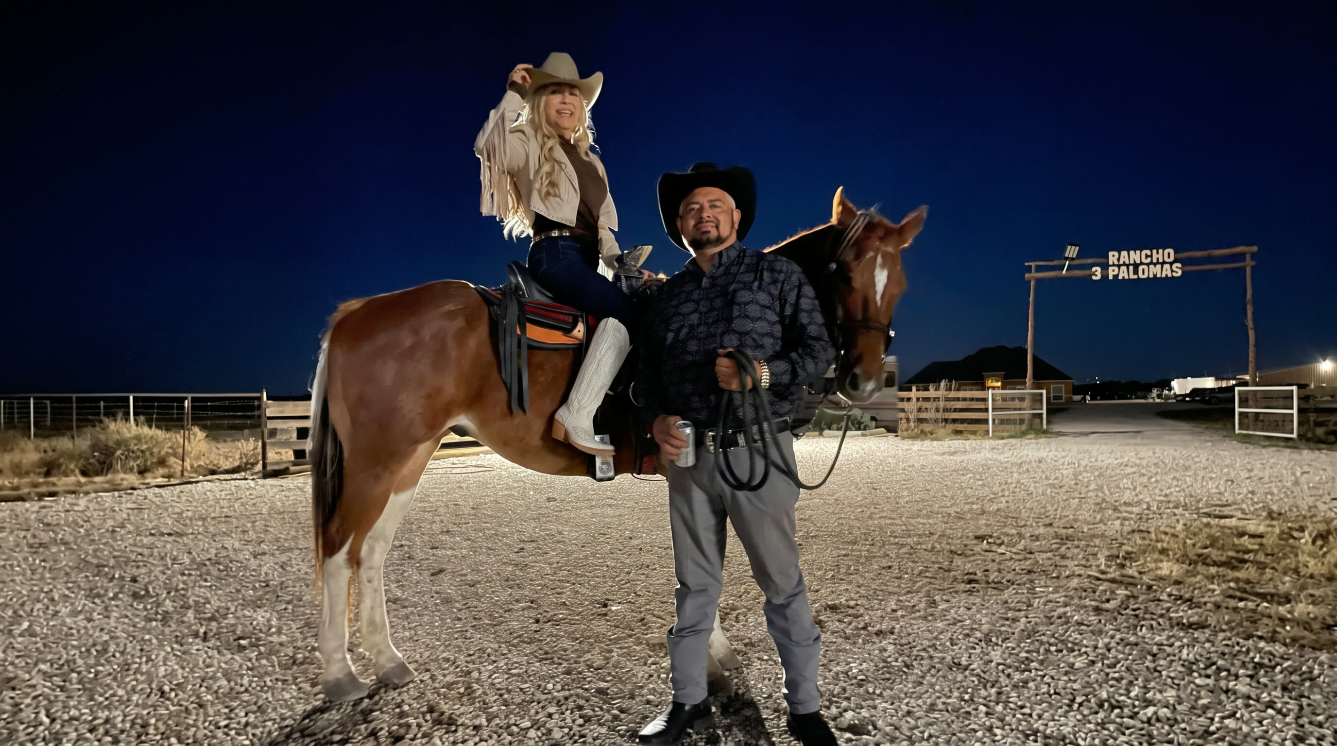 Couple with their horse in front of the lit ranch sign at night