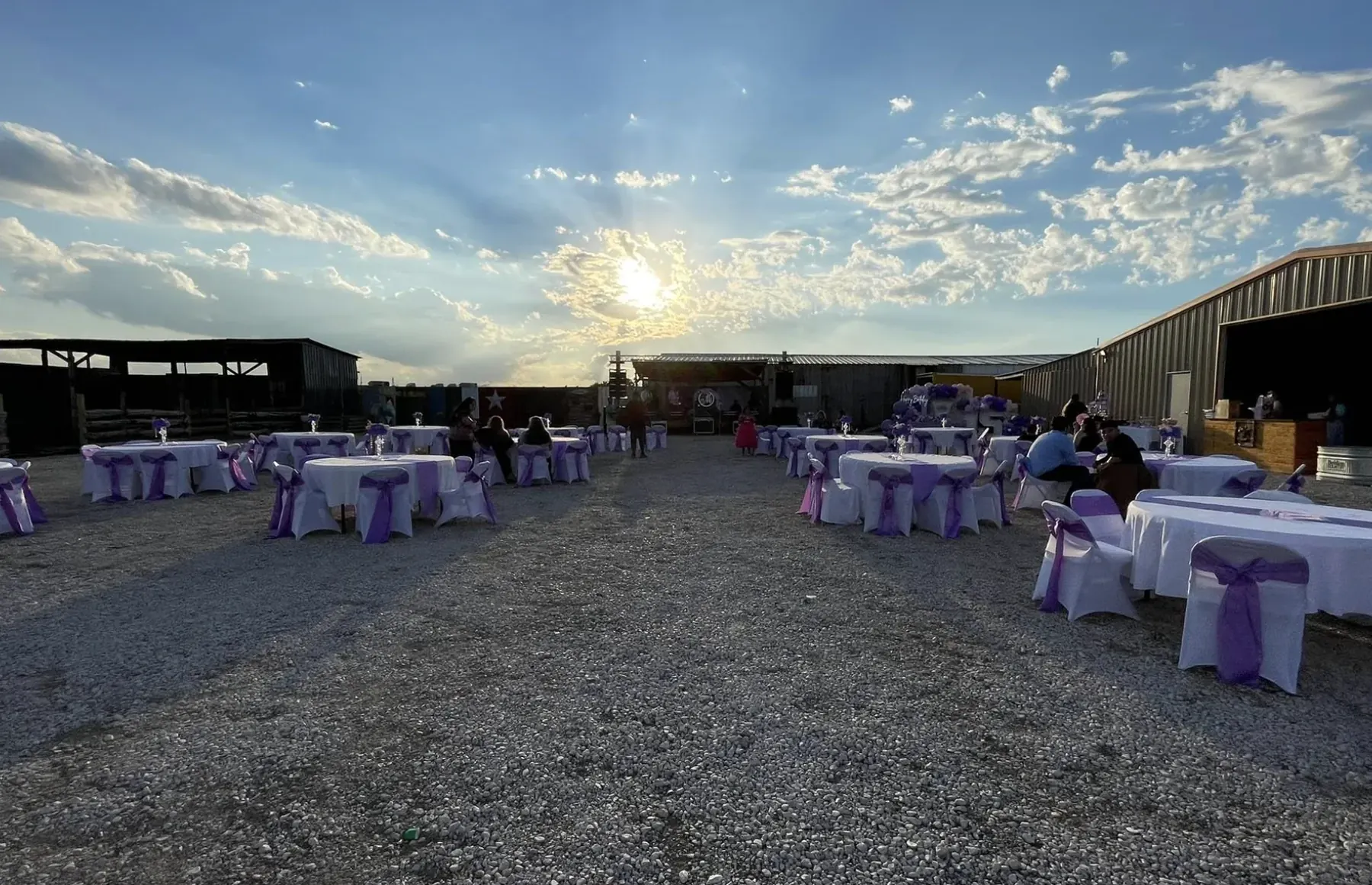 Outdoor tables with purple decorations beneath the sunset sky at Rancho 3 Palomas